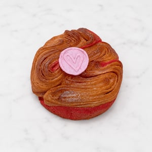 Brioche di San Valentino a forma intrecciata con glassa lucida, dettagli rossi e decorazione rosa a forma di cuore.