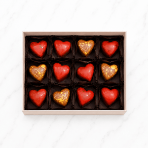 Scatola di praline a forma di cuore rosso e oro, disposte ordinatamente in confezione elegante.