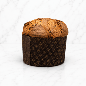 Panettone artigianale natalizio con copertura decorata e gocce di cioccolato, fotografato su sfondo marmo chiaro.