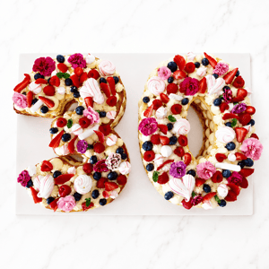 Torta numero “30” decorata con frutti rossi, meringhe, fiori e crema su base moderna da festa.