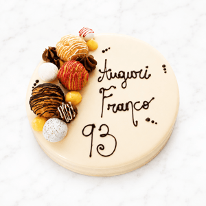 Torta anniversario bianca decorata con bignè, cioccolato e scritta personalizzata “Auguri Franco 93”.