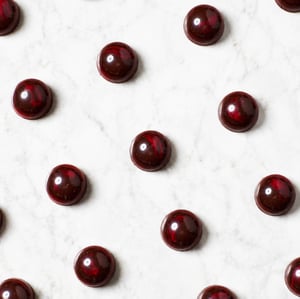 Vista dall’alto di una selezione di praline sferiche di cioccolato fondente con finitura lucida e sfumature rosso rubino, disposte ordinatamente su un piano in marmo bianco